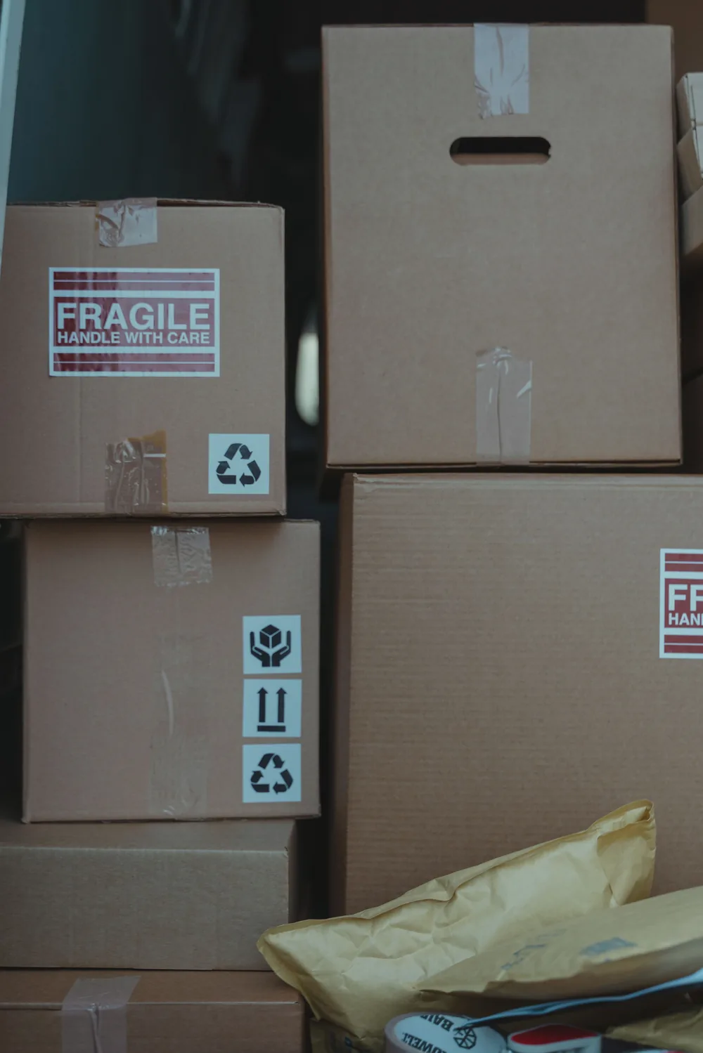 Stack of sealed brown corrugated cartons with FRAGILE labels and universal handling icons including this-way-up, fragile and recycling symbols.